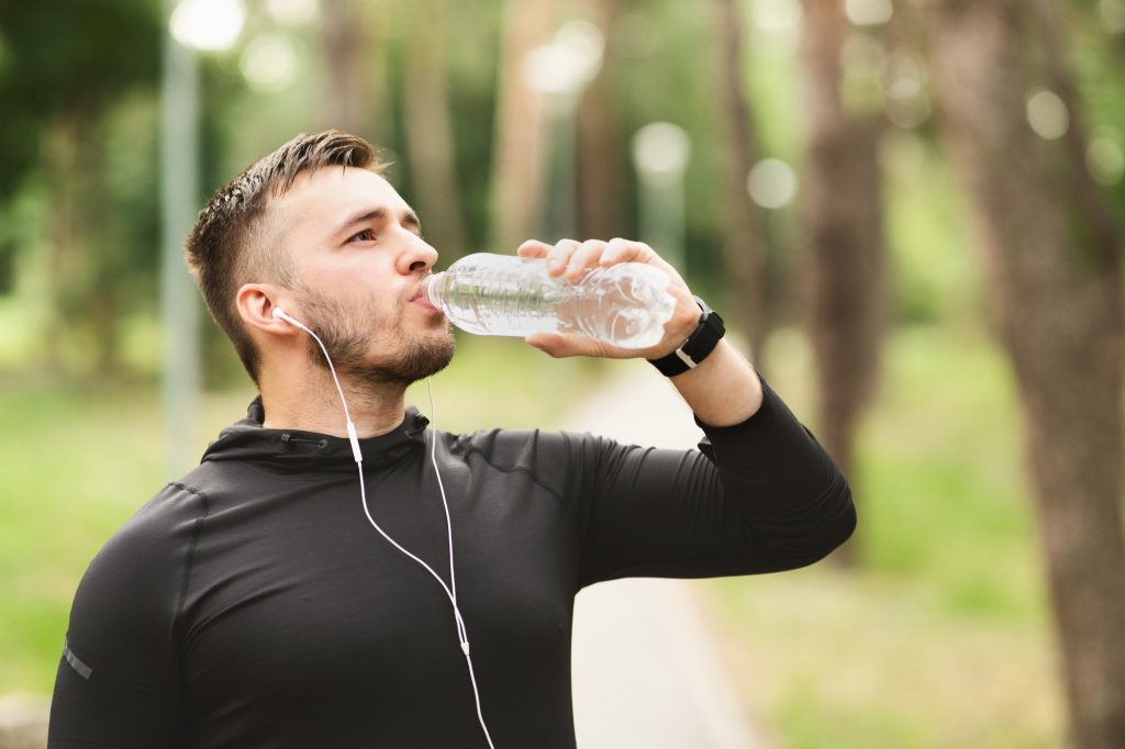 Athletic man drinking water after workout in the park