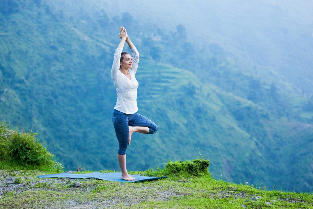 Woman in yoga asana Vrikshasana tree pose outdoors